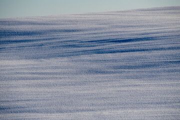 The texture of blue ripples on a snowy field created by wind and light