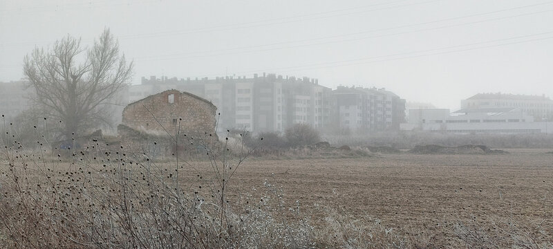 Vista rural de ruinas hist&oacute;ricas junto a campos arados con edificios modernos en la niebla invernal en Burgos, Espa&ntilde;a