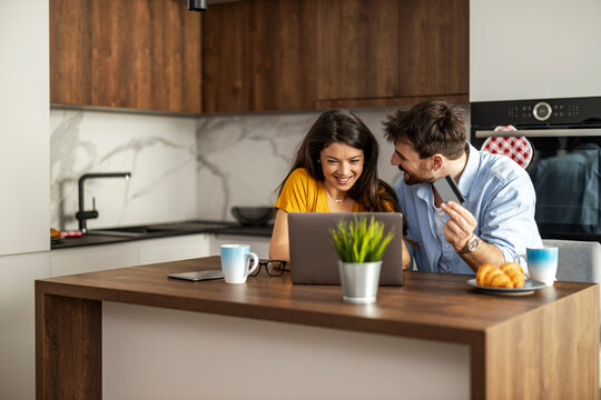 Happy couple enjoying morning coffee and working on a laptop in a modern kitchen setting