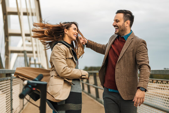 Couple enjoys playful moment on bridge during cloudy day with wind in their hair