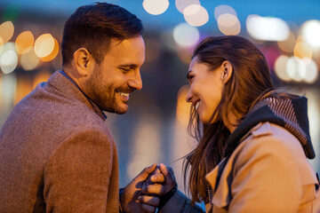 Couple enjoying a romantic moment by the water at dusk with city lights reflecting in the background