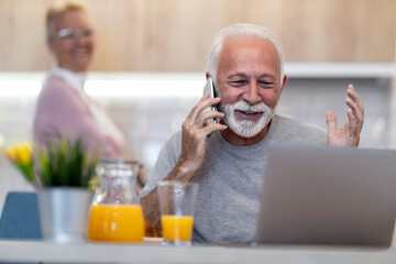 Senior man enjoying a video call with family while sitting at a kitchen table in the morning light