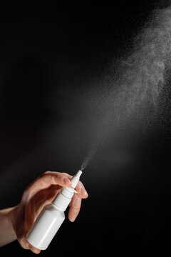 A hand is holding a spray bottle, releasing a fine mist, illustrating the application of vasoconstrictor drops for rhinitis treatment. This method is linked to common respiratory issues.