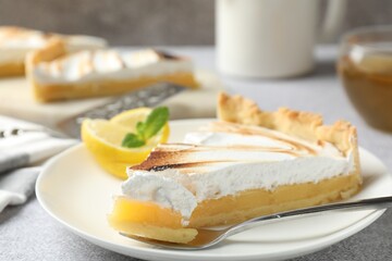 Slice of tasty lemon meringue tart with mint served on light grey table, closeup