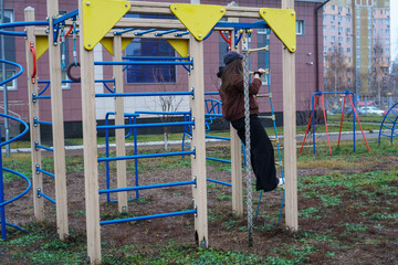 Young woman in casual clothes climbing rope ladder on a colorful outdoor playground. Urban residential background.