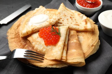 Delicious crepes with red caviar and sour cream on black table, closeup