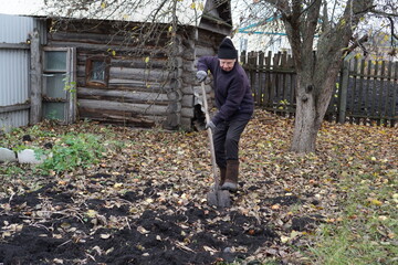 Elderly person digging soil with a shovel in a rustic autumn garden.