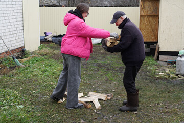 Young woman helping senior man carry firewood in a rural backyard during autumn.