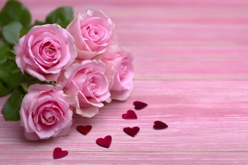 A romantic bouquet of pink roses with hearts, in pastel pink and red, representing a holiday gift on a wooden background, with copy space