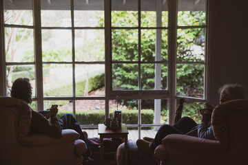 retired couple sit eating in chairs of home by window and garden