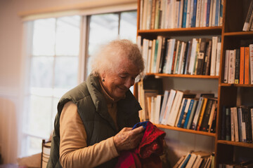 elderly woman smiles in cosy home by bookcase
