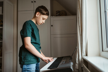 Teen boy standing room and playing an electronic keyboard.