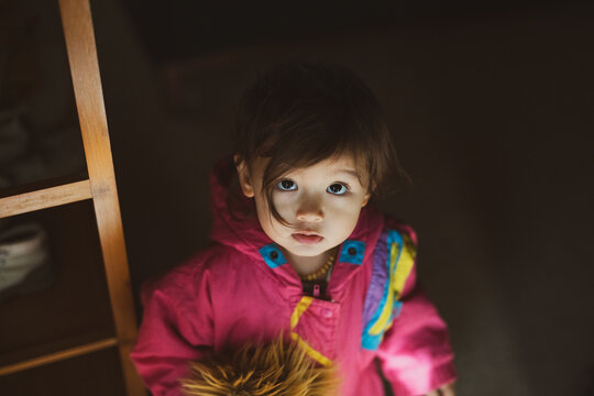 cute mixed-race toddler looks up at home with pink jacket
