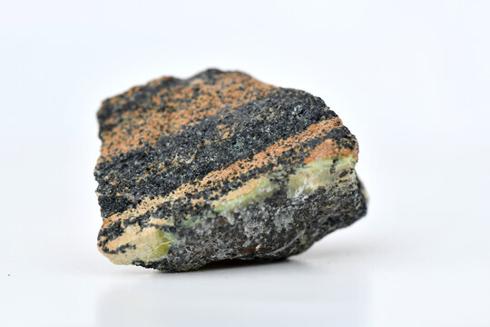 Macro shot of a dark, striated rock specimen with black and orange/brown layers on a reflective white surface, perfect for geology and science concepts.
