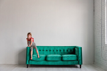 Little girl standing on green sofa in minimalist white room