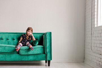 Little girl sits on green sofa in minimal white urban room