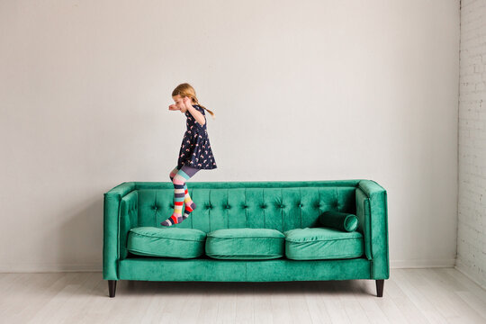 Girl jumping on green sofa in bright minimalist room