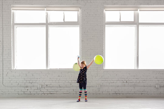 Young girl with balloons stands in white warehouse