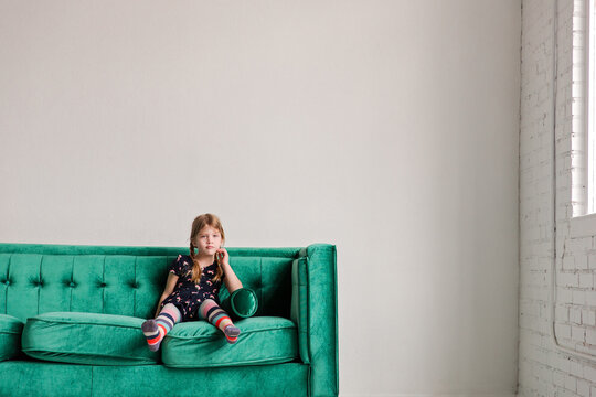 Little girl sitting thoughtfully on velvet couch in bright room
