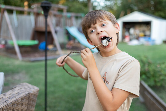 Boy eating a roasted marshmallow on a stick in a backyard setting