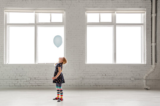 Little girl watching a floating balloon in bright white room