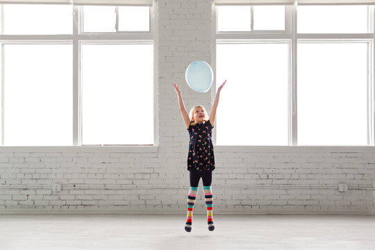 Happy young girl tossing a balloon in a bright white room