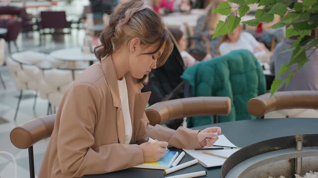 young woman examines palette options at cafe, female shopper picks and tests color swatches leisurely, attentive young woman evaluates different shades on paper while shoppers walk past her