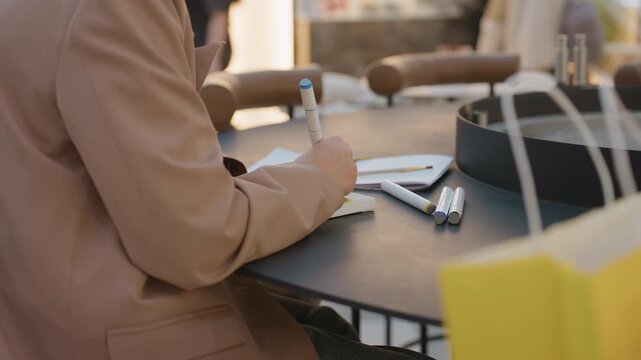 caucasian woman organizing her schedule publicly, closeup of lady jotting notes amid shopping area activities, woman surrounded by shopping bags and writing in her planner at mall table
