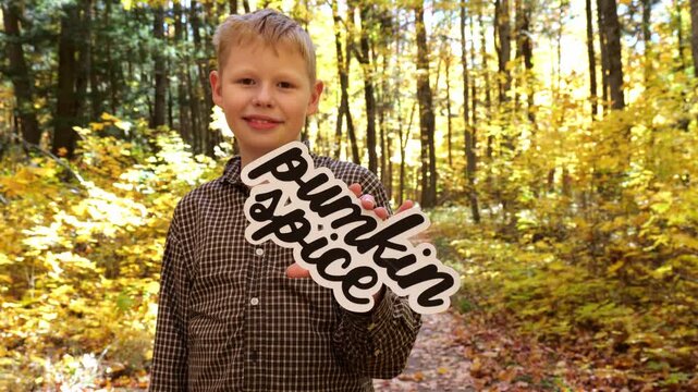 Smiling Boy holds up words Pumpkin Spice in the Forest with Yellow Leaves in the Fall 4K Video Stock Footage