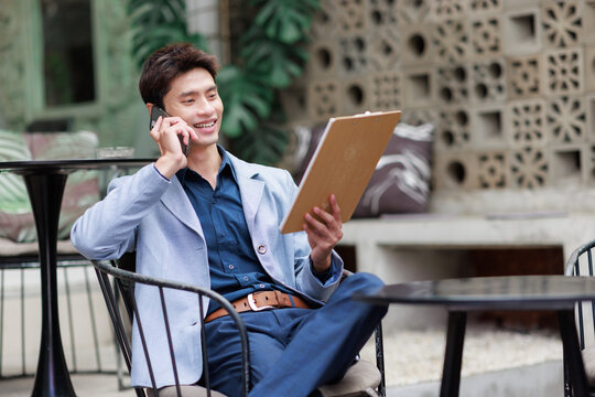 Young asian man discussing business on mobile phone holding clipboard