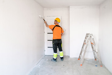 A construction worker paints a wall with a wide, specialized paint roller. Apartment renovation.