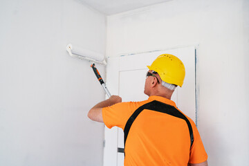A construction worker paints a wall with a wide, specialized paint roller. Apartment renovation.