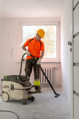 A finishing worker vacuums a floor after sanding it with a specialized construction vacuum cleaner. Apartment renovation.