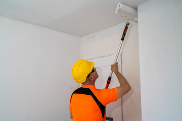 A construction worker paints a wall with a wide, specialized paint roller. Apartment renovation.