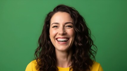 A smiling woman with wavy dark hair looks forward showing teeth against a plain green background wearing a yellow top - Powered by Adobe