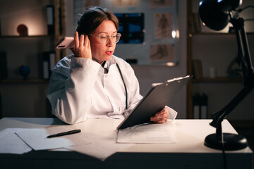 busy young female doctor communication with patients using modern technology, listening to voice message on smartphone working during night shift in hospital