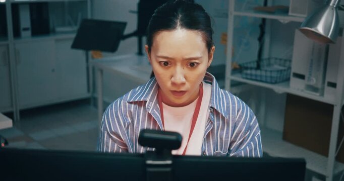 Shocked woman staring at her computer screen with a surprised expression in a dark office.
