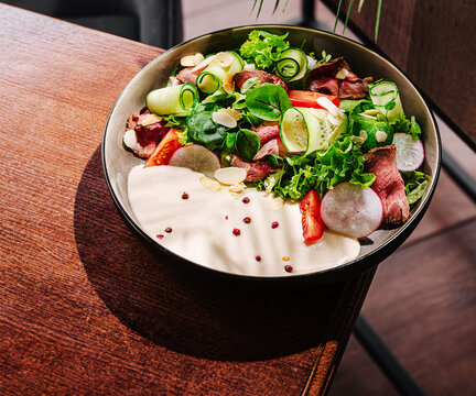 Fresh garden salad with roasted beef on a wooden table at a modern restaurant - Powered by Adobe