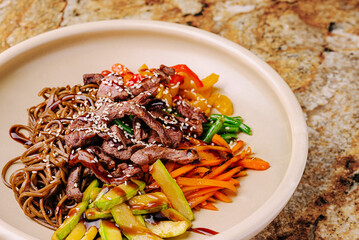 Delicious stir-fried beef with vegetables and noodles on a stone surface