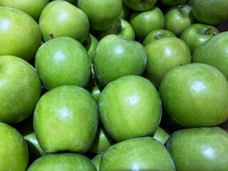 Close-up of shiny green apples piled together, showcasing their fresh and crisp texture at a market or supermarket fruit section.
