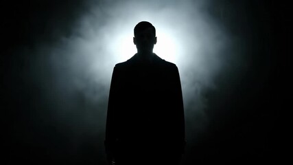 Silhouette of mysterious figure in smoke. Person stands still in dark ambiance, creating suspenseful atmosphere. This captivating moment evokes curiosity and intrigue.