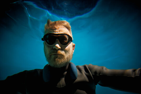 Senior free diver in goggles, neck weight and wetsuit underwater 
