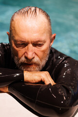 Senior swimmer in diving suit resting at poolside 