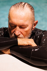 Portrait of grey haired free diver in wetsuit resting at poolside 