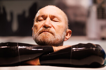 Portrait of grey haired free diver in wetsuit resting at poolside 