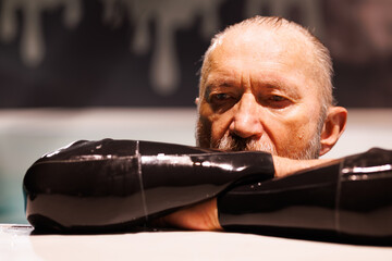 Grey haired diver in wetsuit resting at poolside 