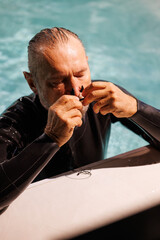 Senior free diver wearing nose clip at poolside during training 