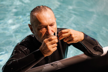 Grey haired diver holding nose clip at poolside 