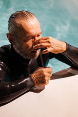 Grey haired diver wearing nose clip at poolside 