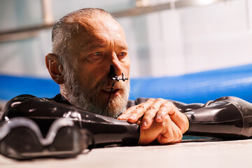 Portrait of senior diver in wetsuit using nose clip near goggles on poolside 